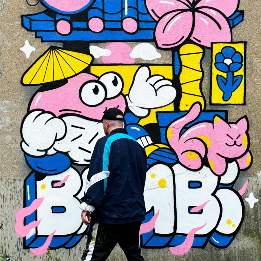 Bambi Bakbi spray painting colorful street art featuring a cartoon character with a mask, a pink cat, and vibrant flowers.