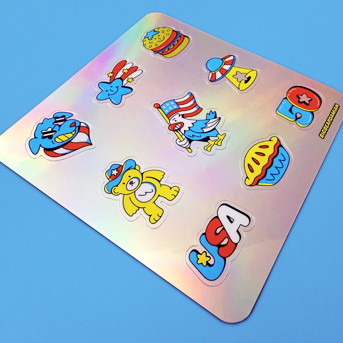Sheet of colorful stickers on a holographic background, featuring patriotic symbols like a bald eagle, USA letters, and various festive designs.