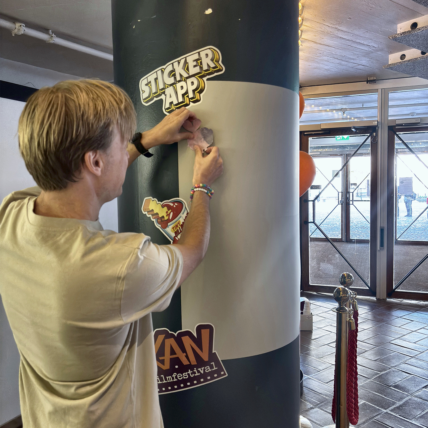 Mann klebt einen Sticker an eine StickerApp-Stickerwand rund um eine Säule beim KAN Film Festival