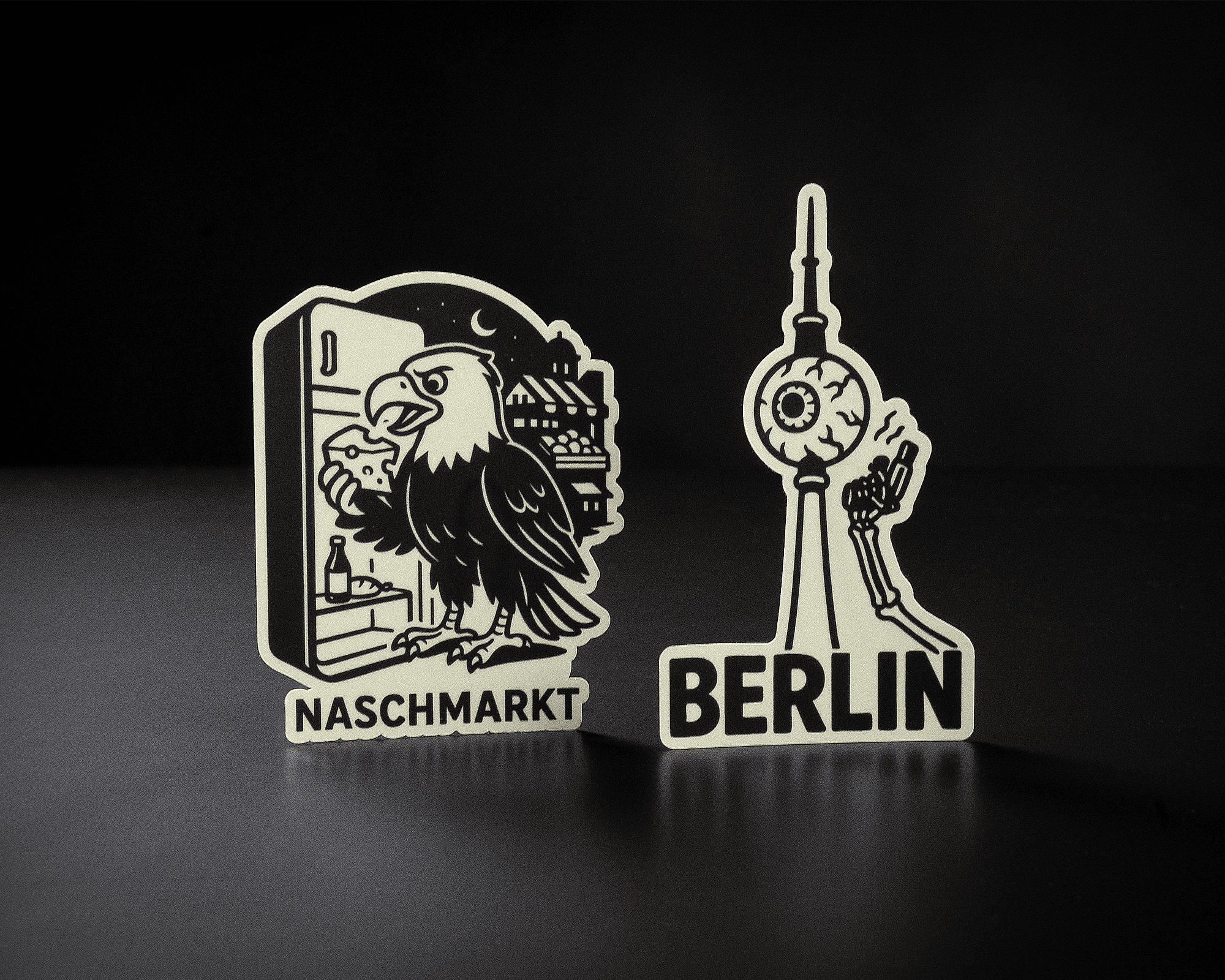 Two black and white stickers: one with an eagle eating a sandwich labeled "Naschmarkt," and the other of the Berlin TV tower labeled "Berlin."