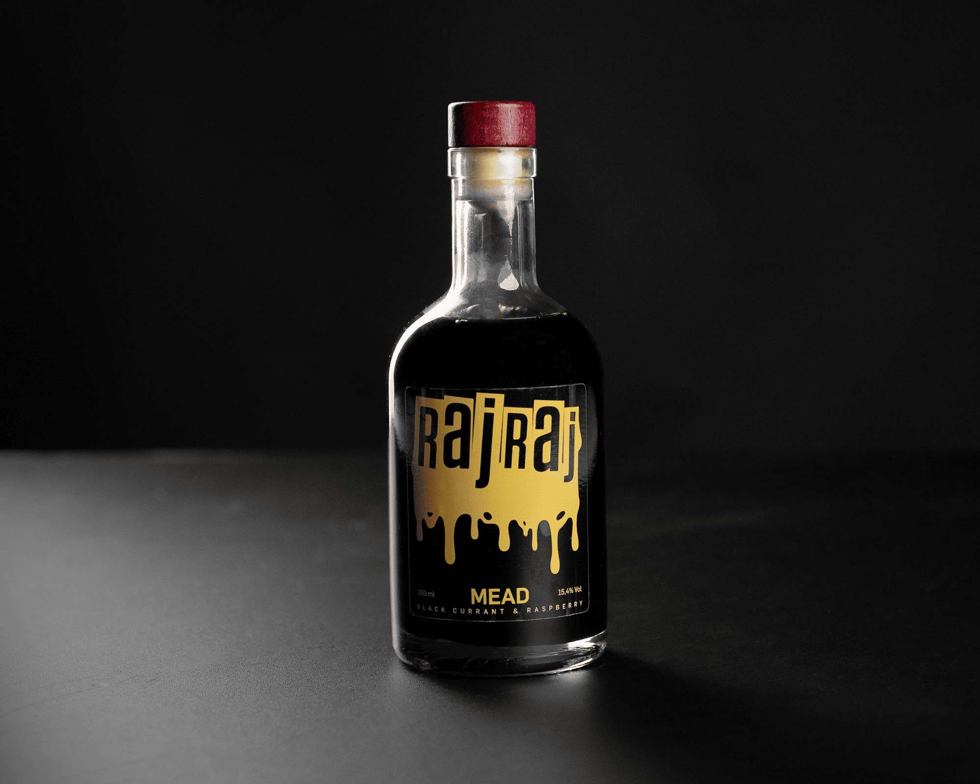 A bottle of dark mead with a red cap, with clear label "RajRaj" and "Black Currant & Raspberry," against a black background.