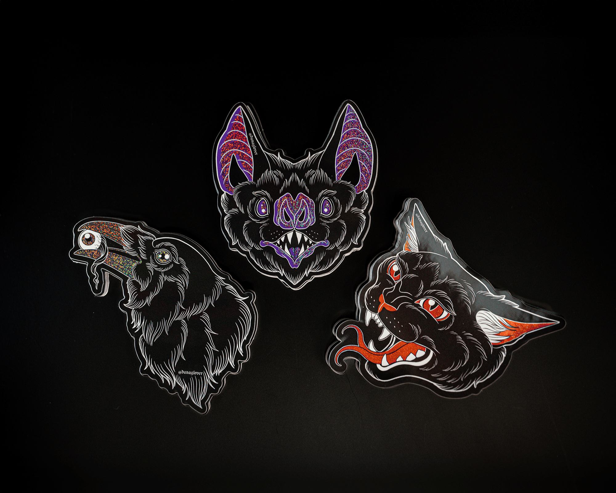 Three colorful, stylized pixie dust stickers on a black background: a bat with purple ears, a bird with a dripping beak, and a snarling cat with red eyes.