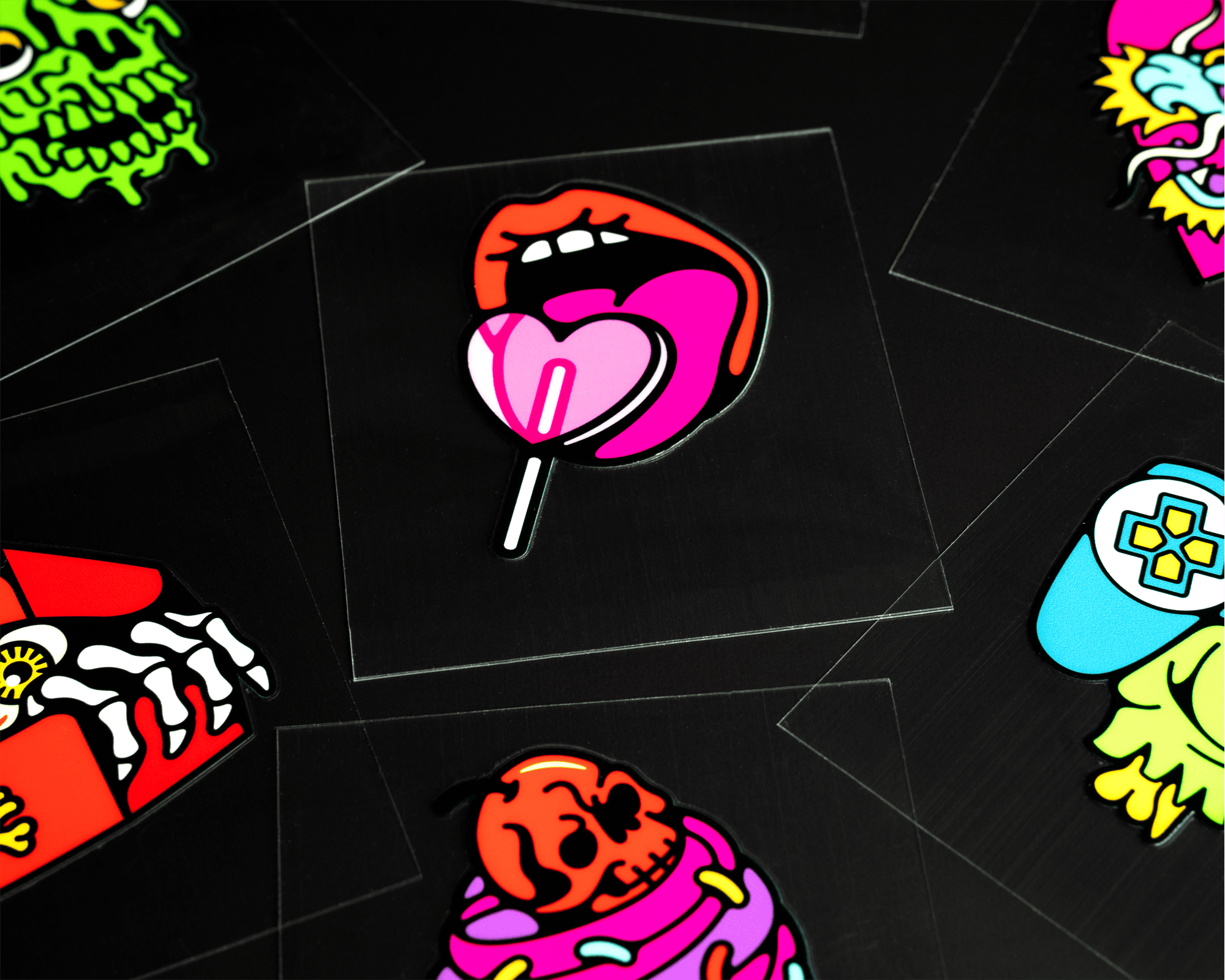 Colorful uv dtf stickers on a black background, featuring a mouth with a lollipop, skulls, and various vibrant designs.