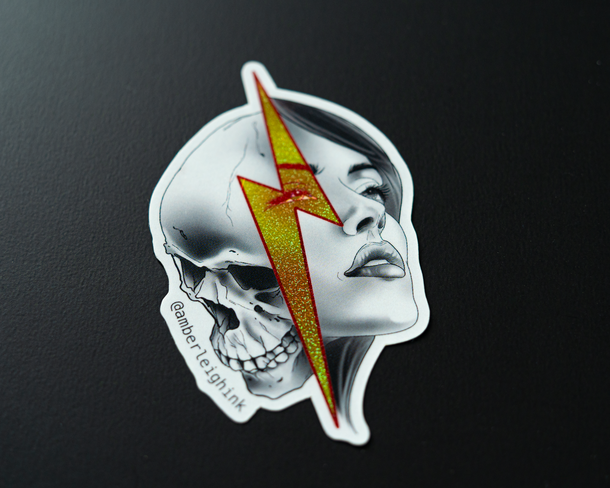 Pixie sticker of a woman's face merging with a skull, crossed by a glittery yellow lightning bolt.