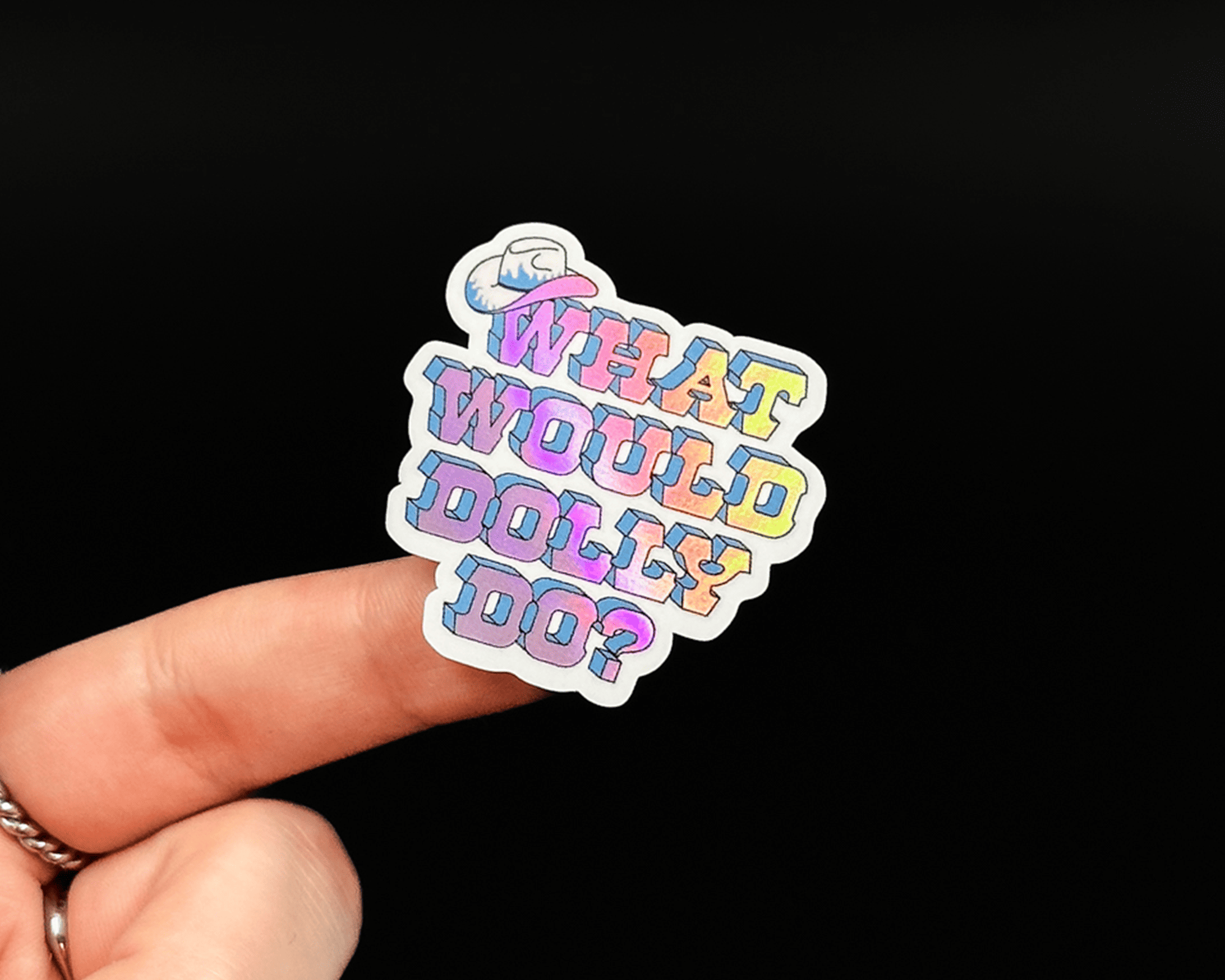Hand holding a holographic sticker with the text "WHAT WOULD DOLLY DO?" against a black background.