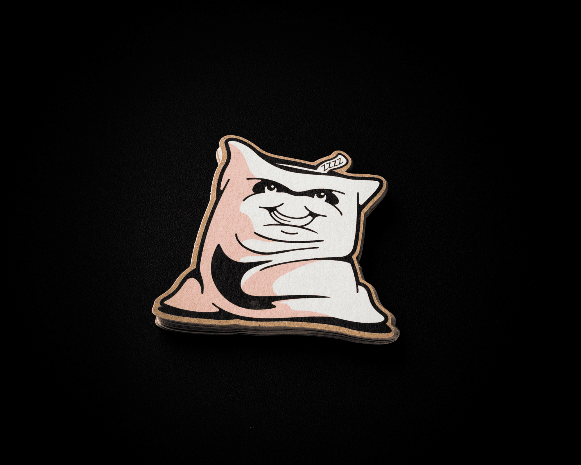 A kraft sticker featuring a cartoon-style pillow with a smiling face on a black background.