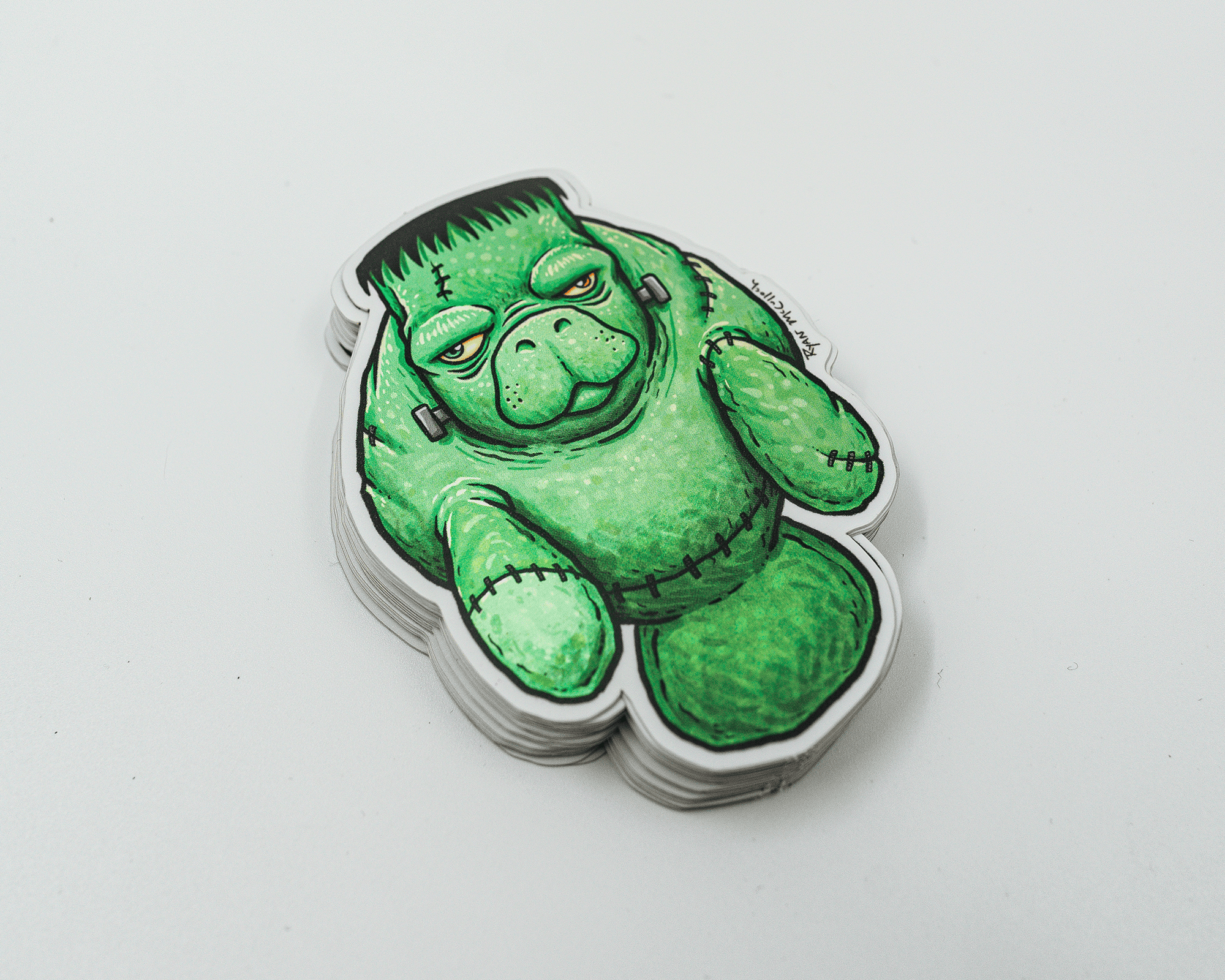 A stack of vinyl stickers featuring a cartoon green creature resembling Frankenstein's monster with a grumpy expression on a white background.