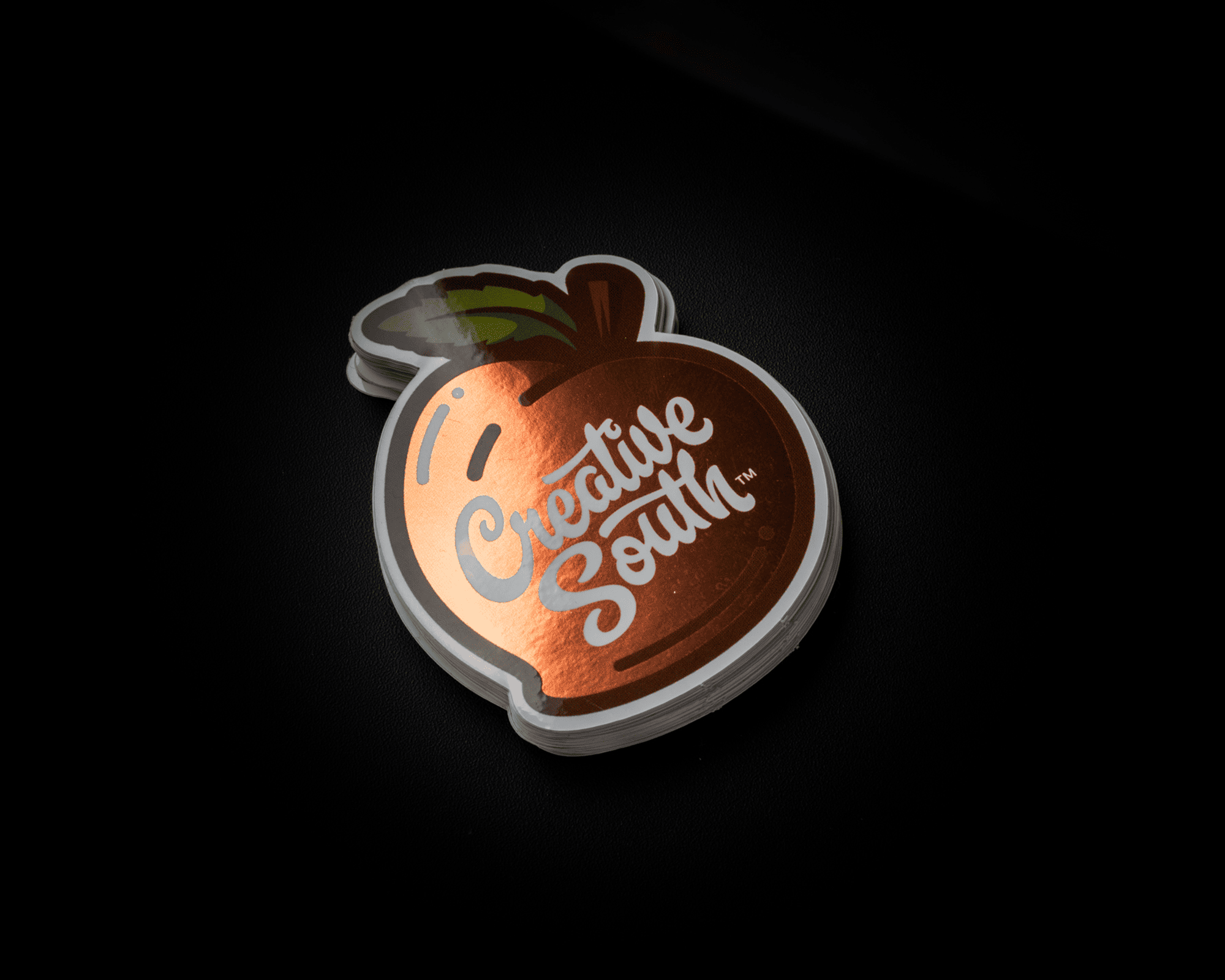 A stack of Creative South mirror stickers featuring a stylized peach with metallic accents on a dark background.