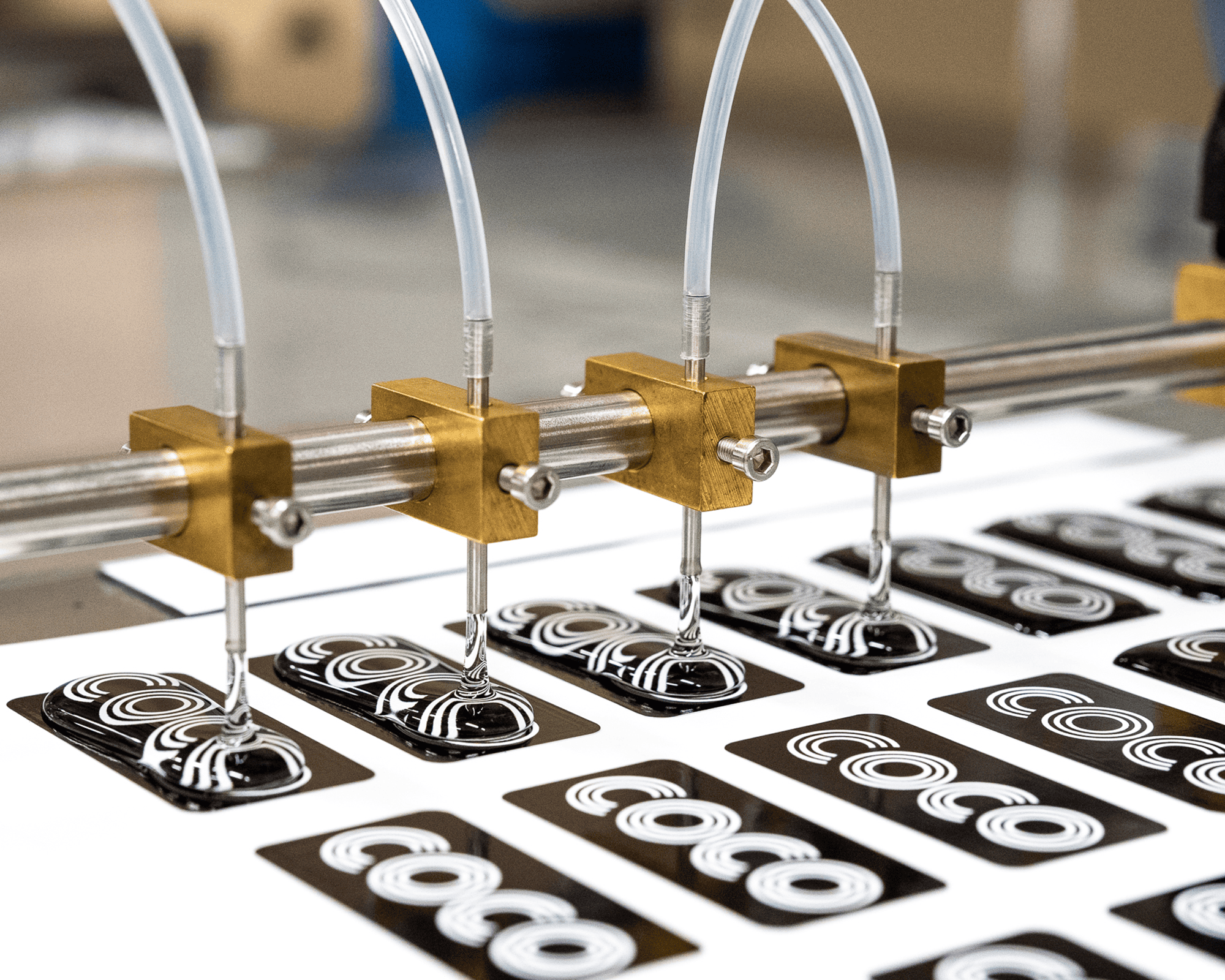 A epoxy machine with four nozzles dispensing intricate black and white patterns onto rectangular cards in a precise, automated process.