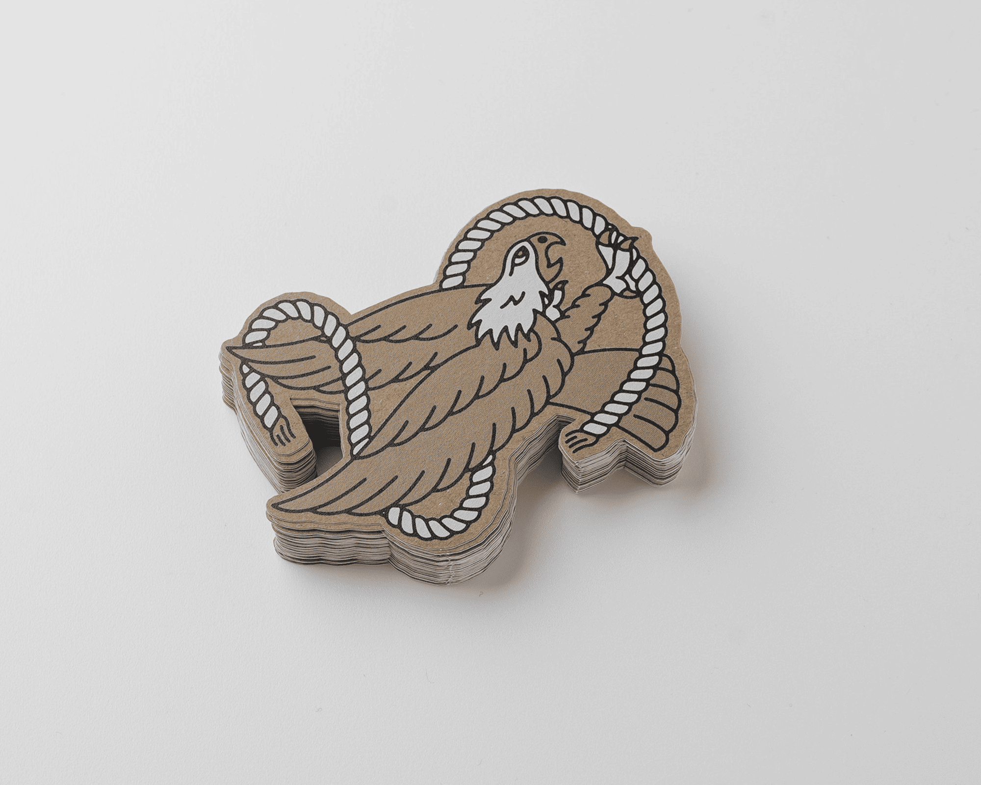Stack of kraft stickers featuring a stylized brown eagle with a white head, holding a rope in its beak, on a white background.