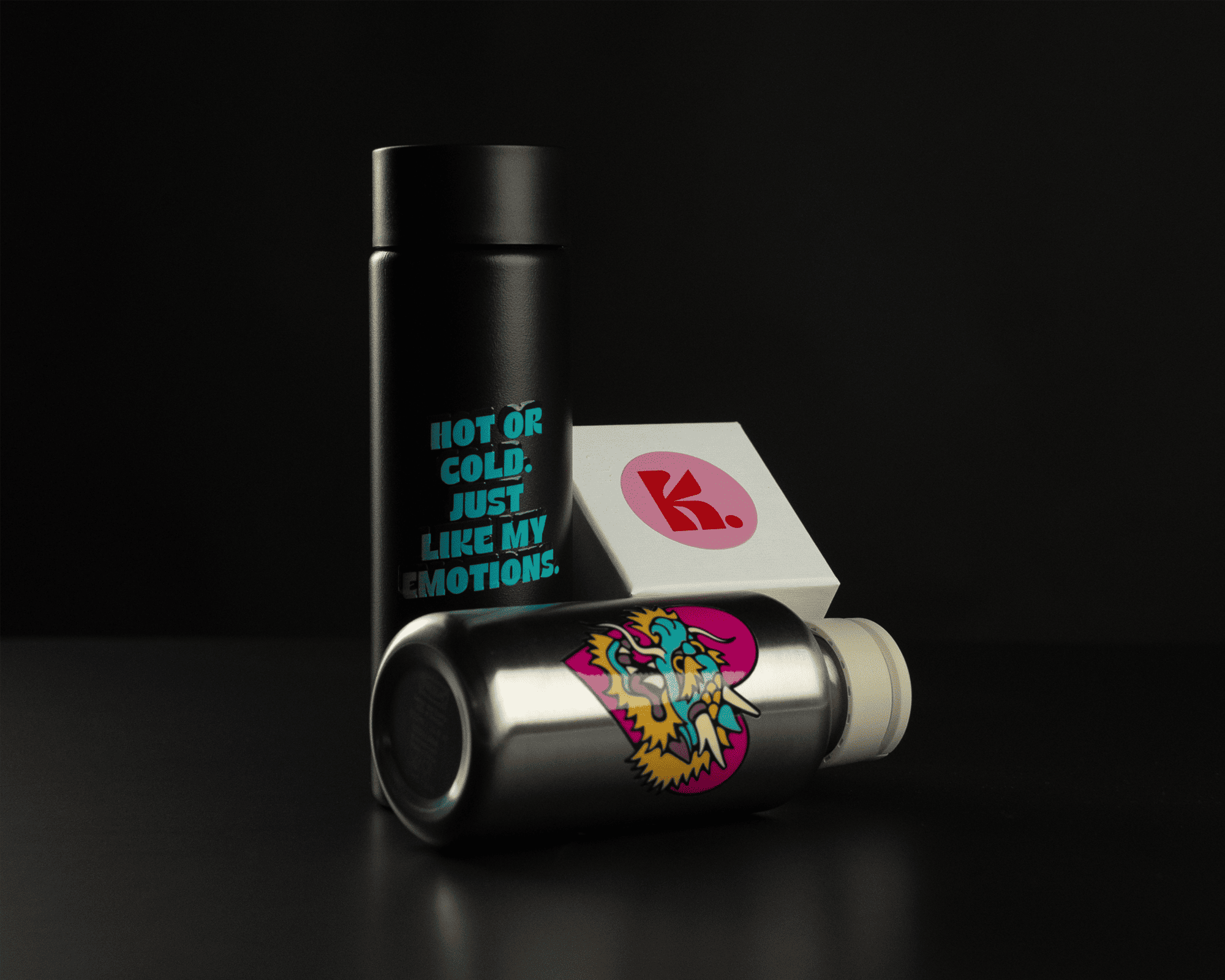 Two stylish thermos bottles, one black with blue text, the other silver with colorful artwork, against a dark background with a card displaying a red logo.