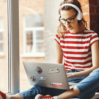 Ein Mädchen sitzt auf einer Fensterbank und benutzt einen Laptop mit individuellen Aufklebern.