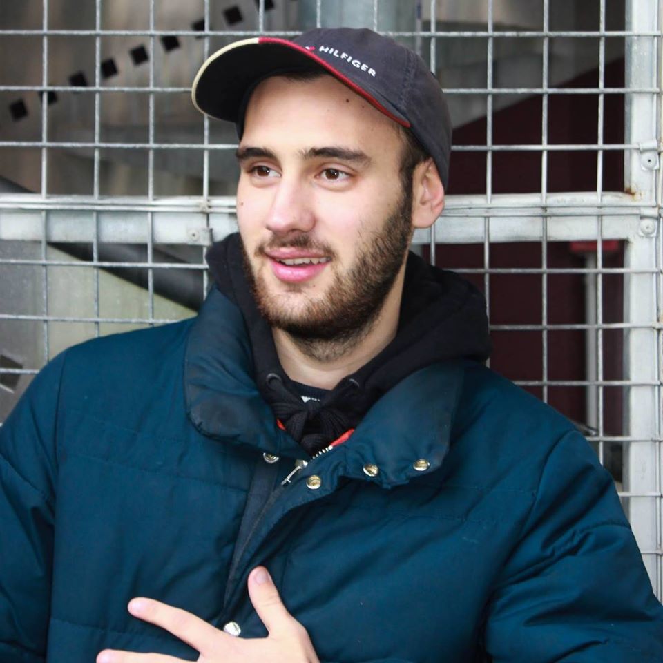 Headshot of Artist of the Month Jenue Woof standing against a fence.